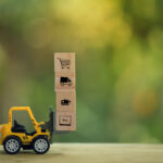 Logistic network distribution and cargo freight concept: Mini fork-lift truck moves a pallet with wooden block with icon. depicts delivering goods or products around globe in e-Commerce.
